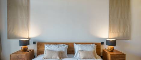 Un dormitorio con cabecera de madera, dos mesitas de noche con lámparas, cama con ropa de cama blanca y una manta decorativa.