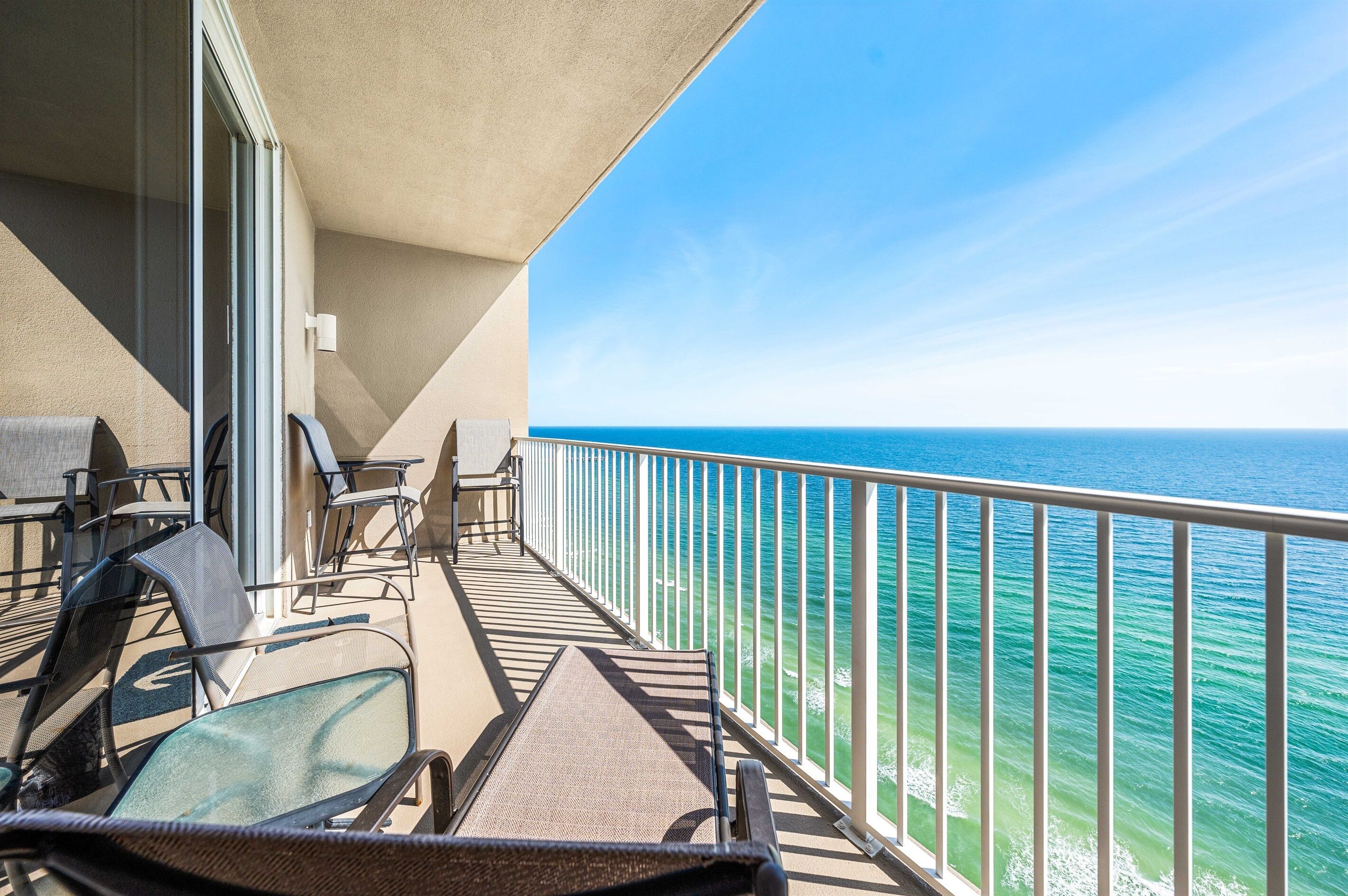 A balcony with chairs and a table, overlooking a clear blue sea.