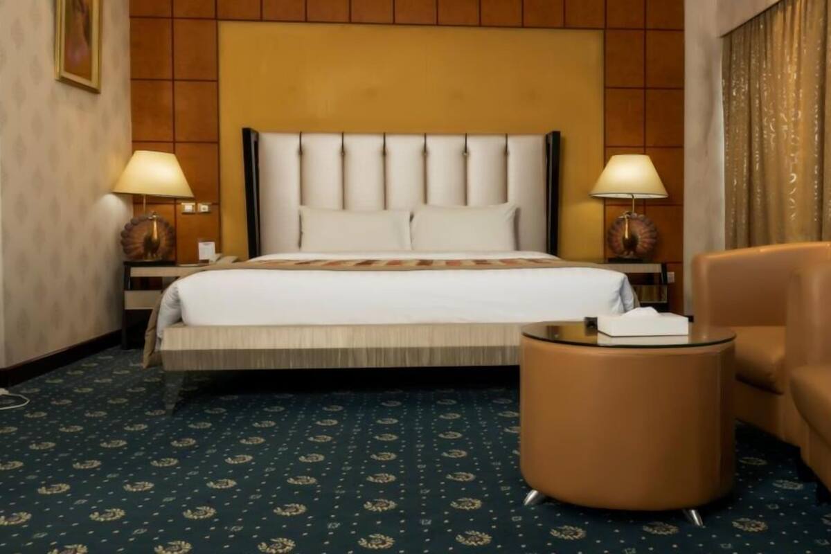 A hotel room with a large bed, two bedside lamps, a round table, and a chair.