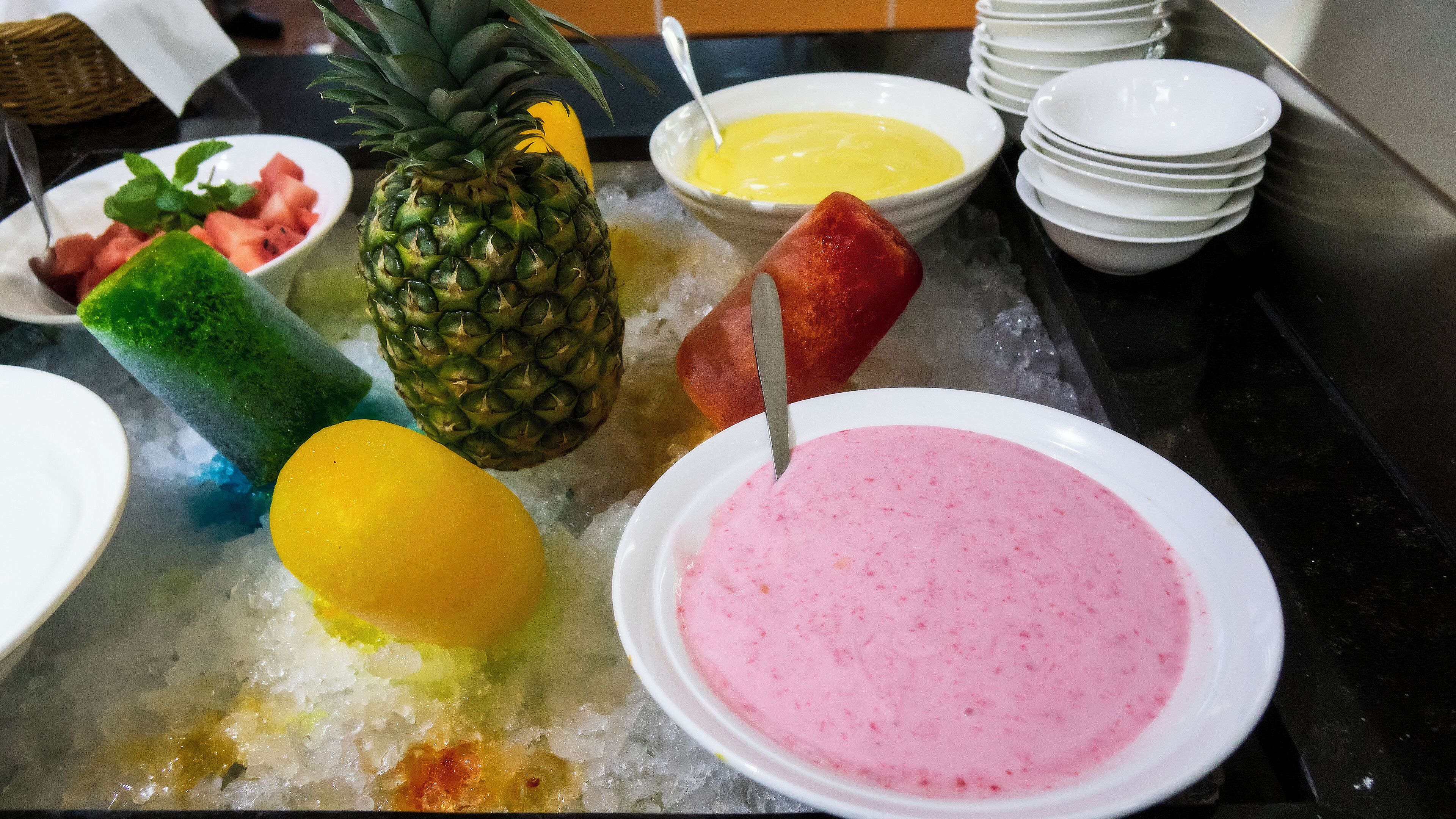 Taula amb diversos aliments, com una pinya, una sandra i bols amb líquids de diferents colors, probablement sucs o batuts.