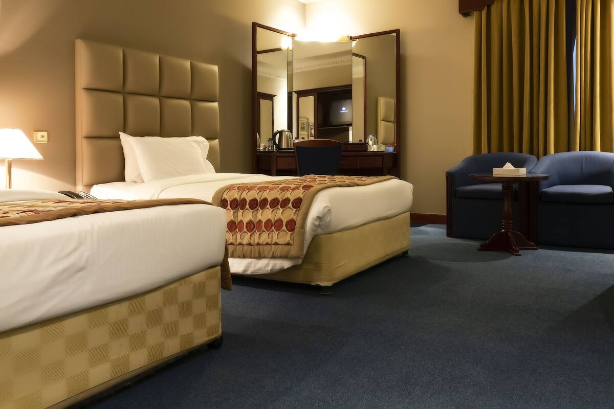 A hotel room with two beds, a large mirror, a television, a small table, and a chair.