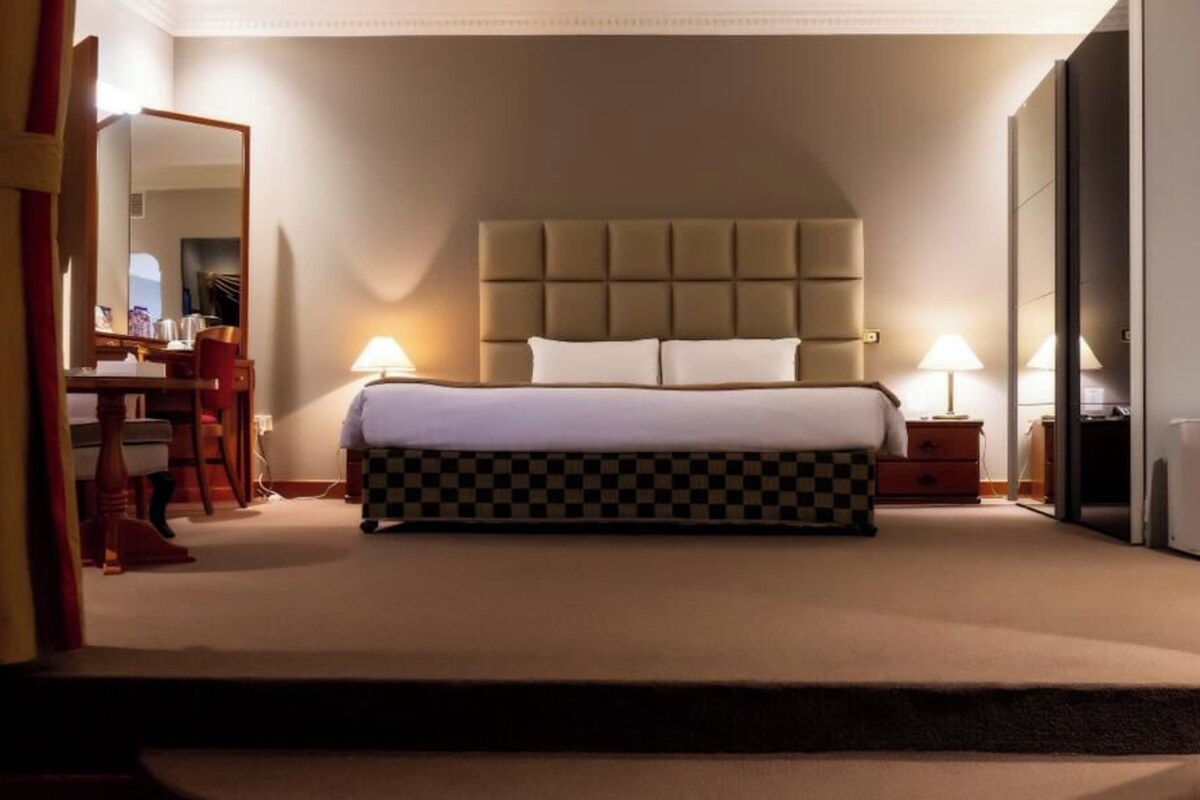 A junior suite with an open living area size of 70 sqm², featuring a large bed, bedside tables, a desk, and a chair.