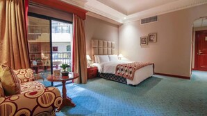A hotel room with a bed, a sofa, a small table with a vase, and a window with curtains. - Panorama Hotel and Spa (Manama)