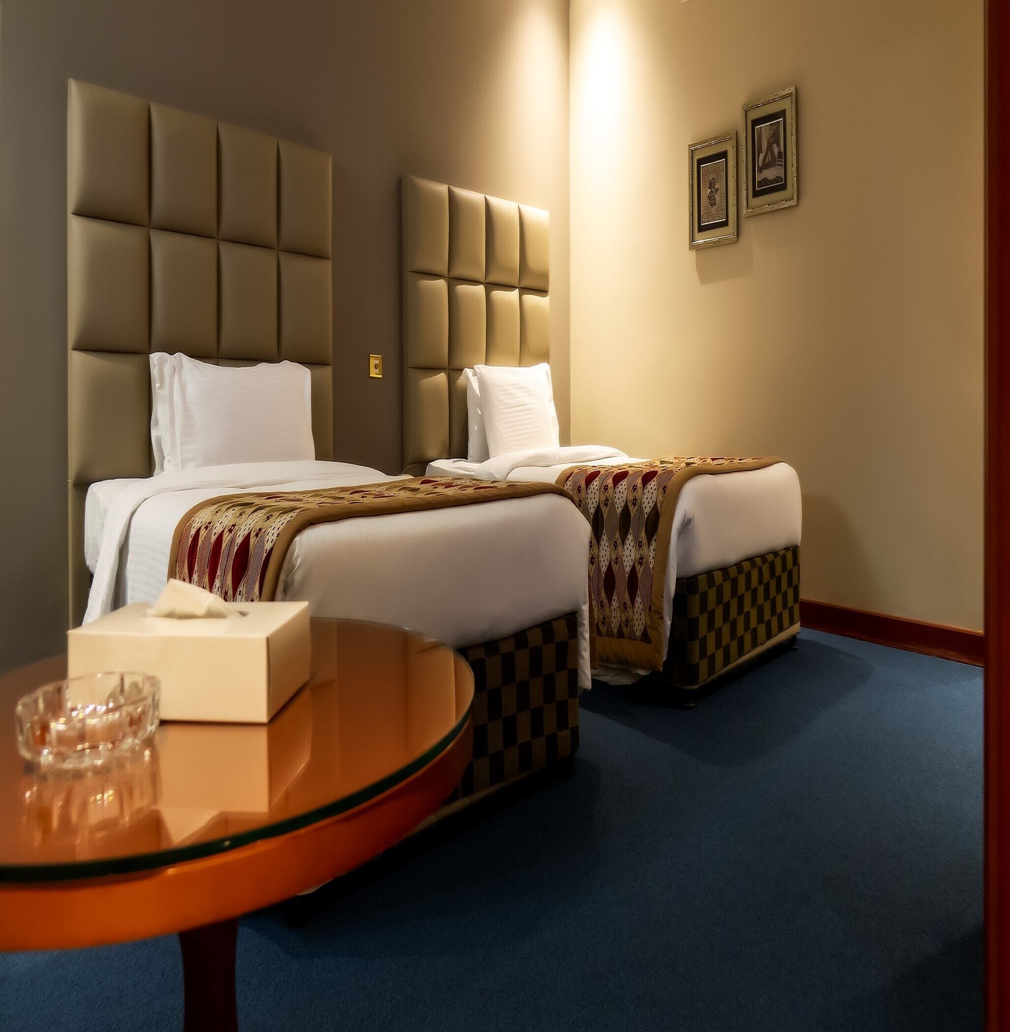 A hotel room with two beds, a round table with a tissue box, and a checkered bed runner.