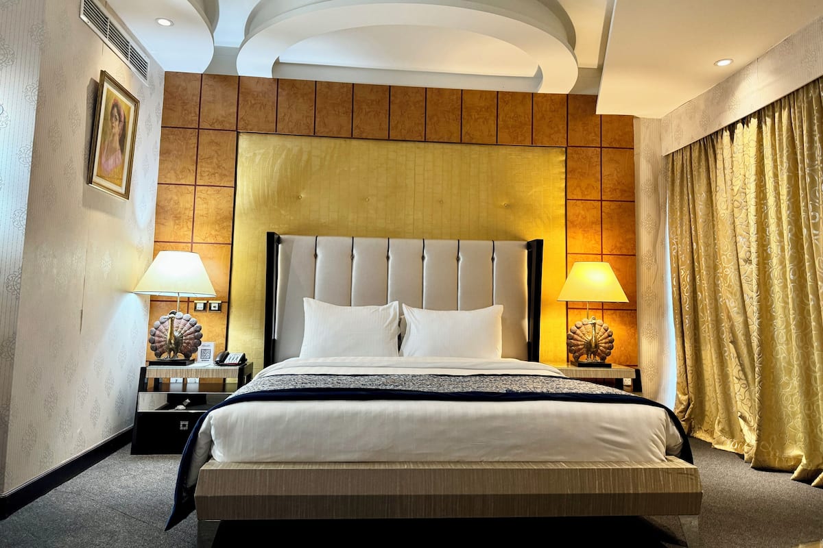 A hotel room with a large bed, two bedside tables with lamps, a headboard, and a curtain.