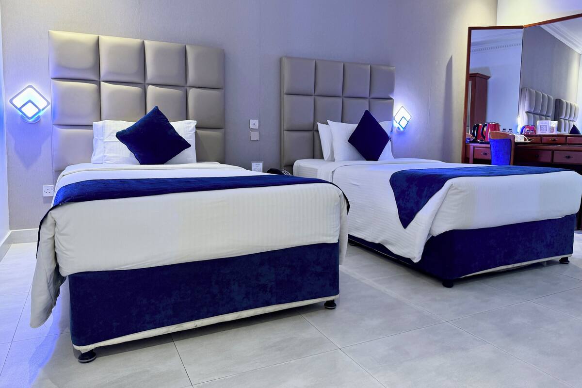 A hotel room with two beds, each with a headboard and pillows, a desk with a chair, and a mirror.