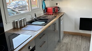 Una cocina compacta con horno integrado, un lavamanos y ventana con vista a un estacionamiento.