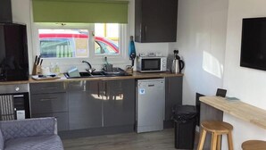 Un espacio habitable compacto con kitchenette, cama, televisor y ventana con vista a la calle.