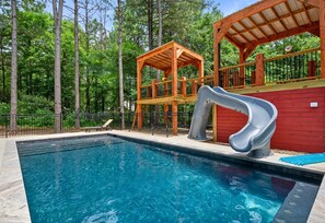 A swimming pool with a slide, wooden deck, and a fenced area.
