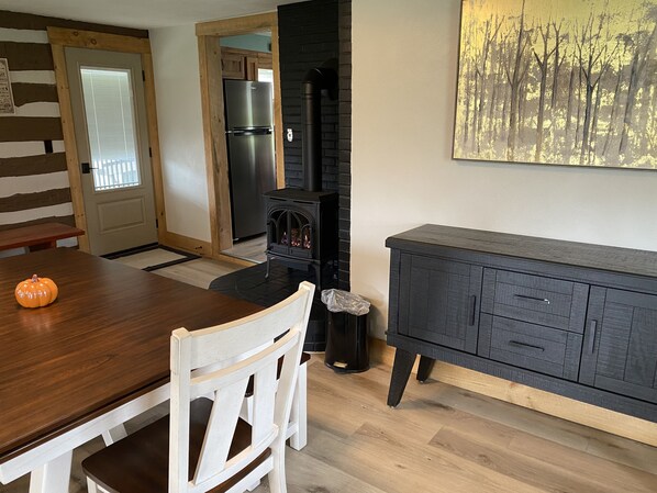 A dining area with a wooden table and chairs, a black stove, and a dark wooden cabinet. - New Listing! Remodeled log farmhouse with lake view! (Huntingdon)