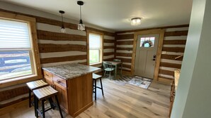 Interior d'una cabana de fusta amb cuina, terres de fusta i una taula de dinar amb cadires.