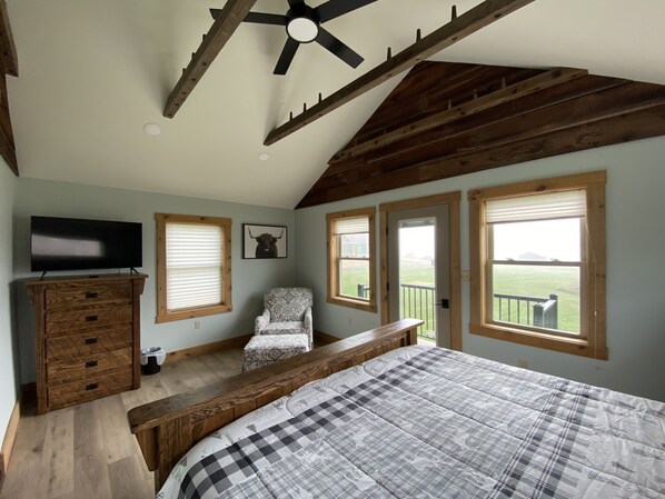 A bedroom with a large bed, a TV, a chair, and a ceiling fan.