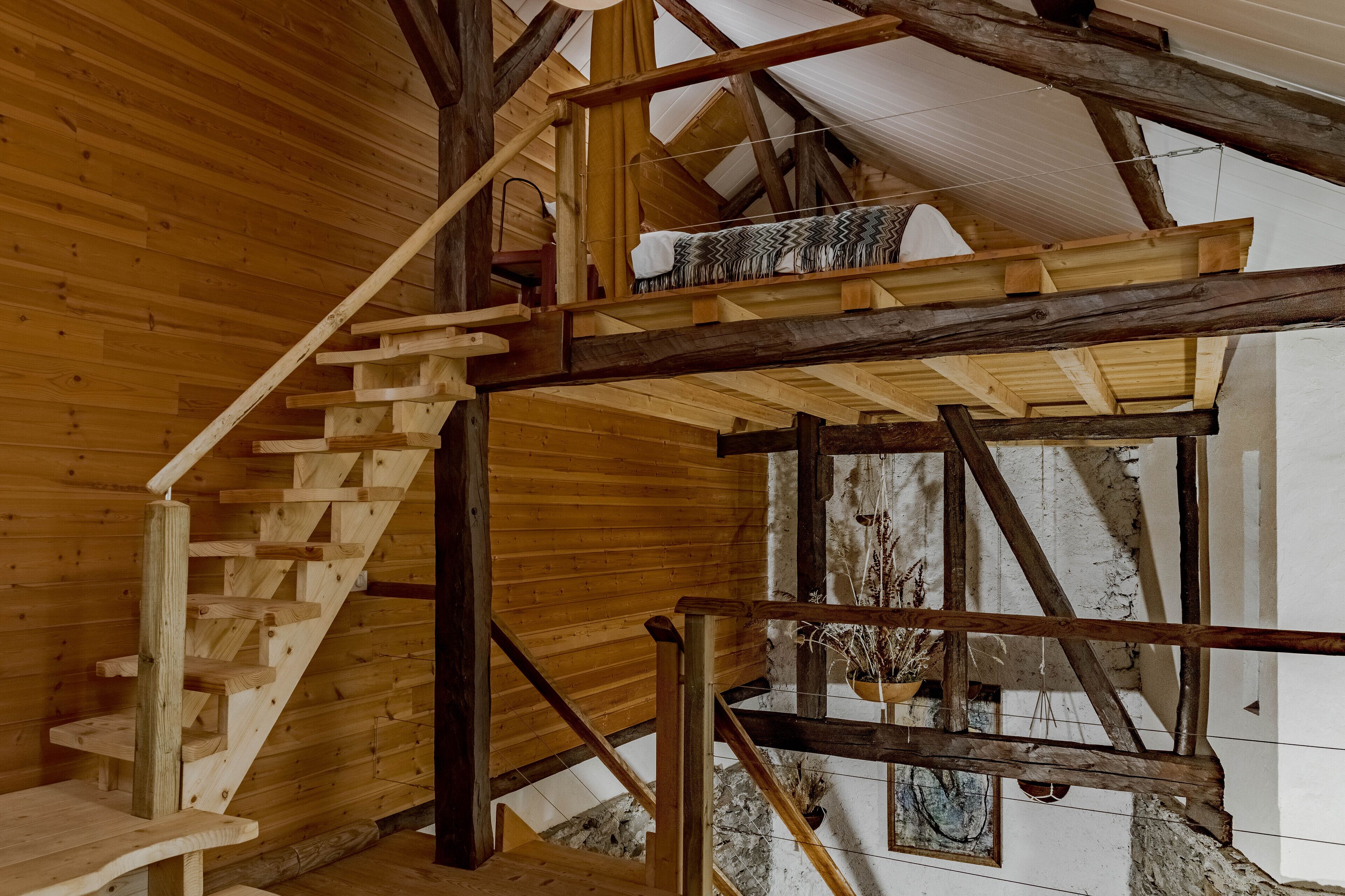 Un escalier en bois au design rustique, menant à une mezzanine agrémentée d’une plante suspendue.