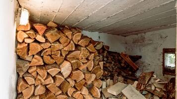A room with a large stack of firewood against the wall and a window with a view of greenery outside.