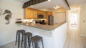A kitchen with a central island, wooden cabinets, stainless steel appliances, and a tiled floor.
