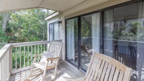 A covered outdoor deck with wooden rocking chairs and a glass door leading to a balcony.