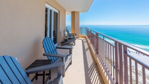 A balcony with blue Adirondack chairs, a table, and a view of the ocean. - Beachfront ~ Private Balcony ~ Golf Cart (Miramar Beach)