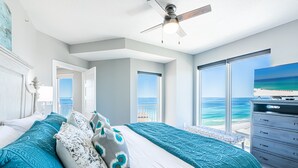 A bedroom with a large bed, a ceiling fan, a TV, and a view of the ocean. - Beachfront ~ Private Balcony ~ Golf Cart (Miramar Beach)
