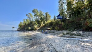 A beach with a house on a hill, clear water, and trees. - Private & secluded beach front on Lake Huron! (Cheboygan)