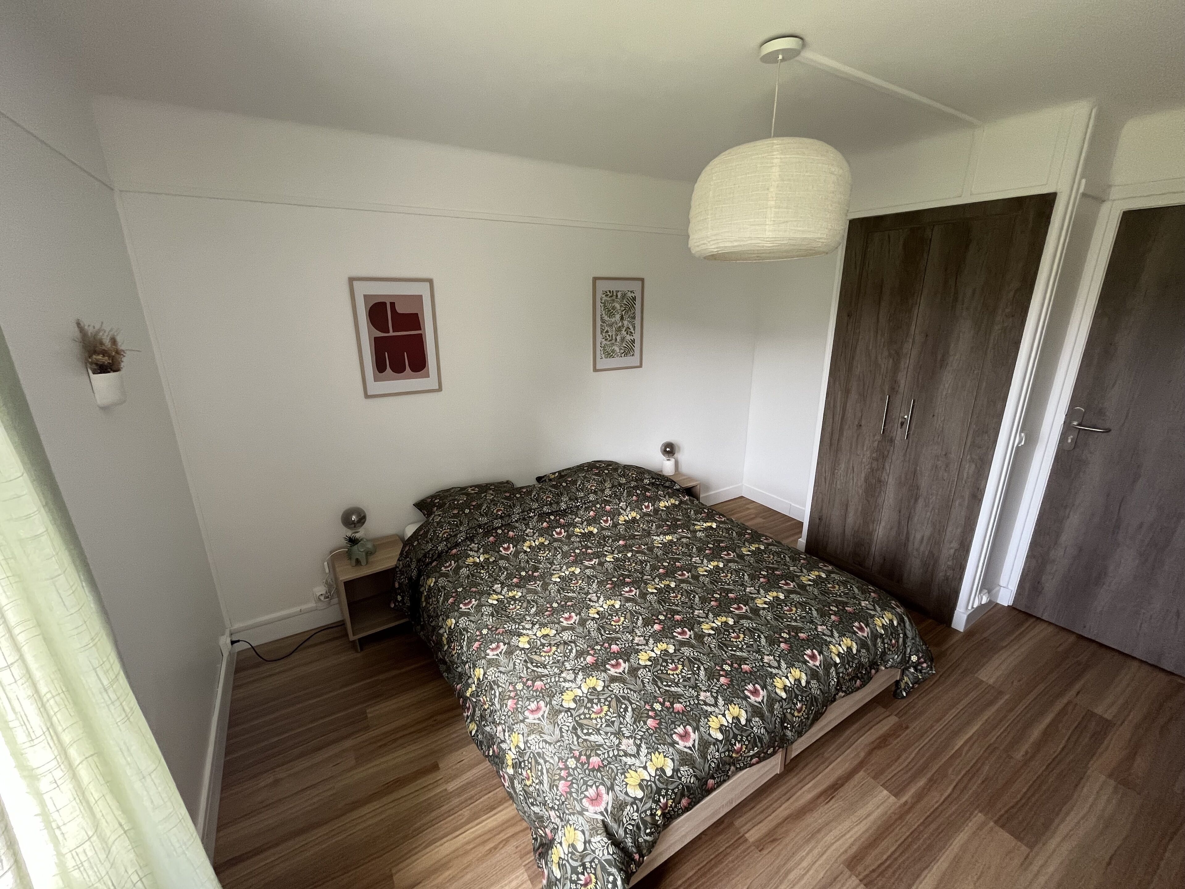Een slaapkamer met een bed, een kledingkast, een nachtkastje en een hanglamp.