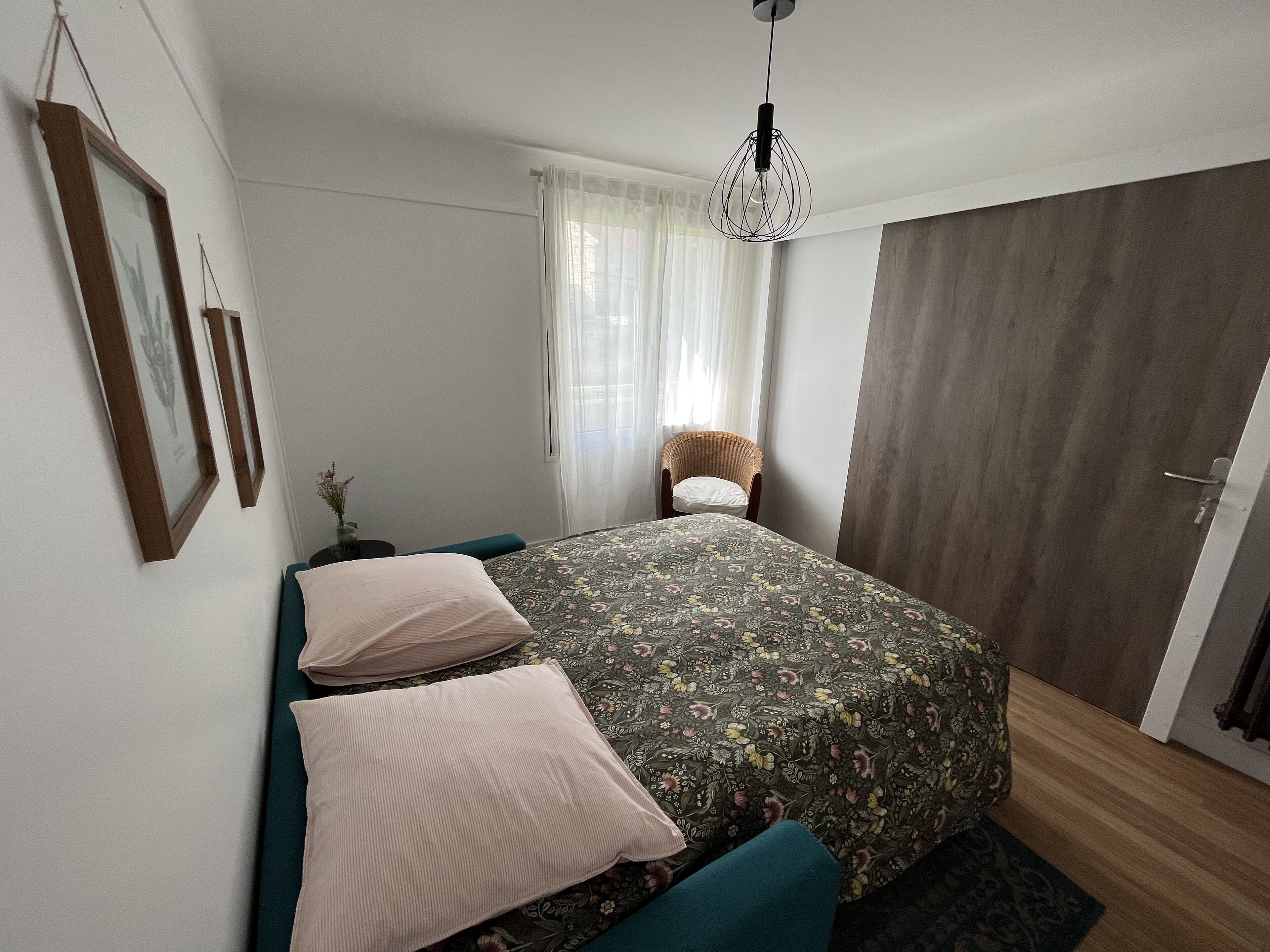 Une chambre à coucher avec un lit, des oreillers, une chaise, un luminaire suspendu et une porte.