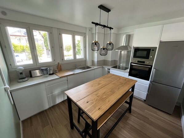 A modern kitchen with white cabinets, a wooden table, a stainless steel refrigerator, and a window with a view of greenery. - A 5 Minutes à Pied de Nombreux Attractions ! Ideal Pour les Familles (Reims)