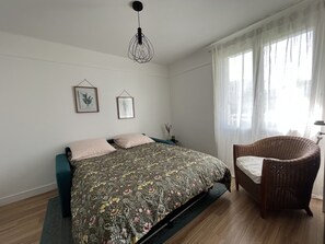 A bedroom with a bed, a chair, a hanging light fixture, and two framed pictures on the wall. - A 5 Minutes à Pied de Nombreux Attractions ! Ideal Pour les Familles (Reims)