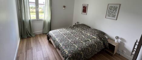 A bedroom with a bed, a bedside table, a hanging light fixture, and a window with curtains.