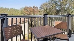 Una terraza de madera con una mesa y sillas, rodeada por una barandilla metálica.