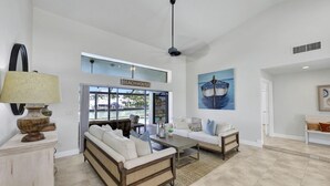 A spacious living room with a sofa set, a coffee table, and a view of the beach through a glass door. - Direct Boating Access | Waterfront Home w/ Pool/Spa (Marco Island)