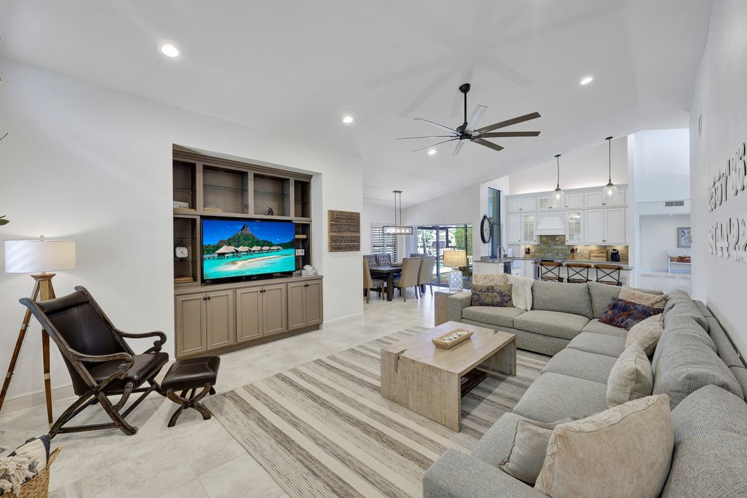 A modern living room with a flat-screen TV, a sofa, a coffee table, and a dining area in the background.
