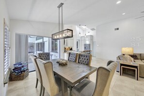 A modern dining area with a wooden table and upholstered chairs, a chandelier, and a view into the kitchen. - Direct Boating Access | Waterfront Home w/ Pool/Spa (Marco Island)