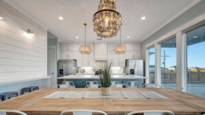 Une cuisine moderne avec des meubles blancs, une table à manger en bois et un grand lustre.