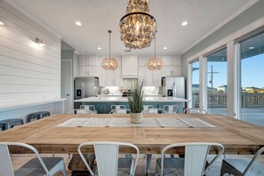 A modern kitchen with white cabinets, a wooden dining table, and a large chandelier.