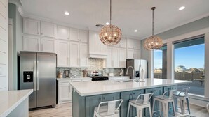Une cuisine moderne avec des meubles blancs, un grand îlot central doté de tabourets, des appareils électroménagers en acier inoxydable et une vue dégagée grâce à de grandes fenêtres.