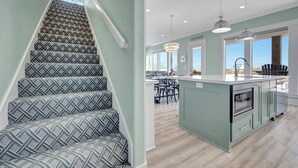 A staircase with patterned carpet, a kitchen with a central island, and a dining area with chairs. - Sunny & 75: 5  BR, 5.5  BA House in Crystal Beach, Sleeps 26 (Bolivar Peninsula)