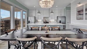 A modern kitchen with a central island, pendant lighting, and a view through large windows. - Sunny & 75: 5  BR, 5.5  BA House in Crystal Beach, Sleeps 26 (Bolivar Peninsula)