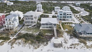 Eine Küstenwohngegend mit mehreren direkt am Strand gelegenen Häusern, die Balkone und Terrassen besitzen und durch Wege miteinander verbunden sind, umgeben von Vegetation.