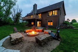 A two-story house with a deck, outdoor seating, and a fire pit.