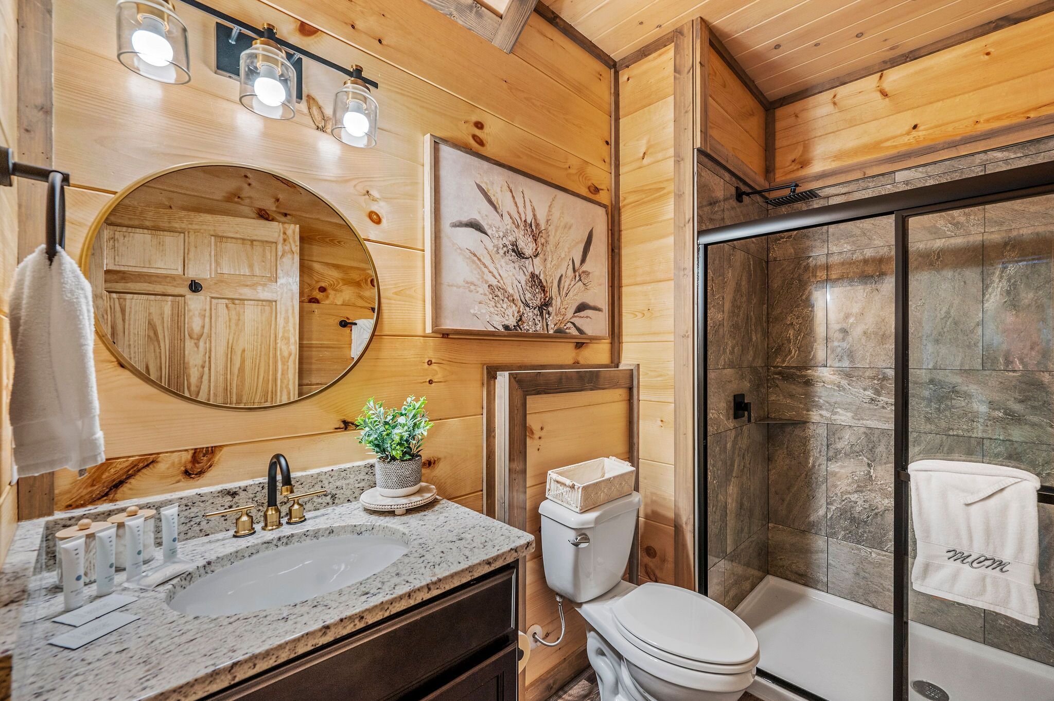 Un baño de madera con lavamanos, espejo, inodoro y ducha.