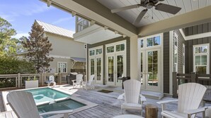 A covered outdoor deck with a pool, white Adirondack chairs, and a ceiling fan.