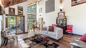 A spacious living room with a sofa, armchairs, and a coffee table. There are large windows, a wooden ceiling, and a deer head mounted on the wall.