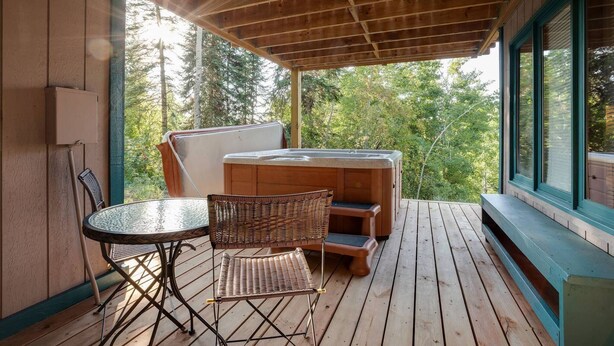 A covered outdoor area with a hot tub, wicker chairs, and a table.