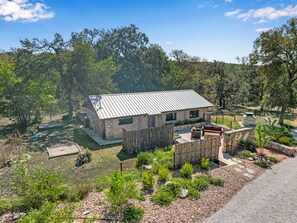 A rustic stone house with a metal roof, surrounded by a wooden fence and small shrubs.