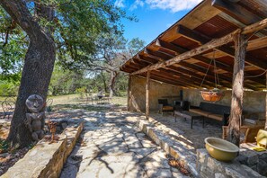 A rustic outdoor seating area with stone pathways, wooden furniture, and a hanging basket.
