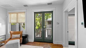 A room with a wooden floor, a chair with a cushion, a small round table, and a door leading outside.