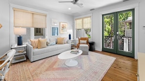 A living room with a white sofa, a coffee table, a ceiling fan, and a view of the outdoors through large windows.