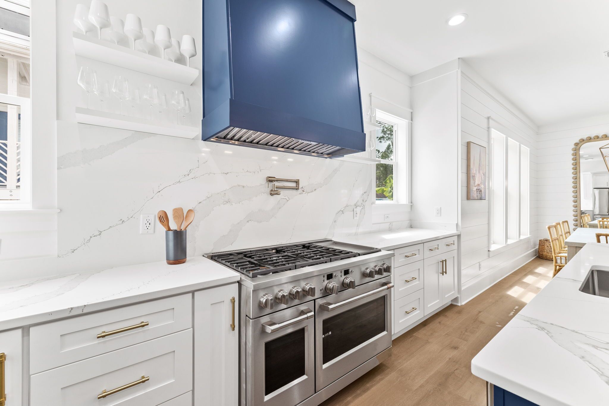 Une cuisine moderne avec des meubles blancs, une cuisinière en acier inoxydable et une hotte de couleur bleue.