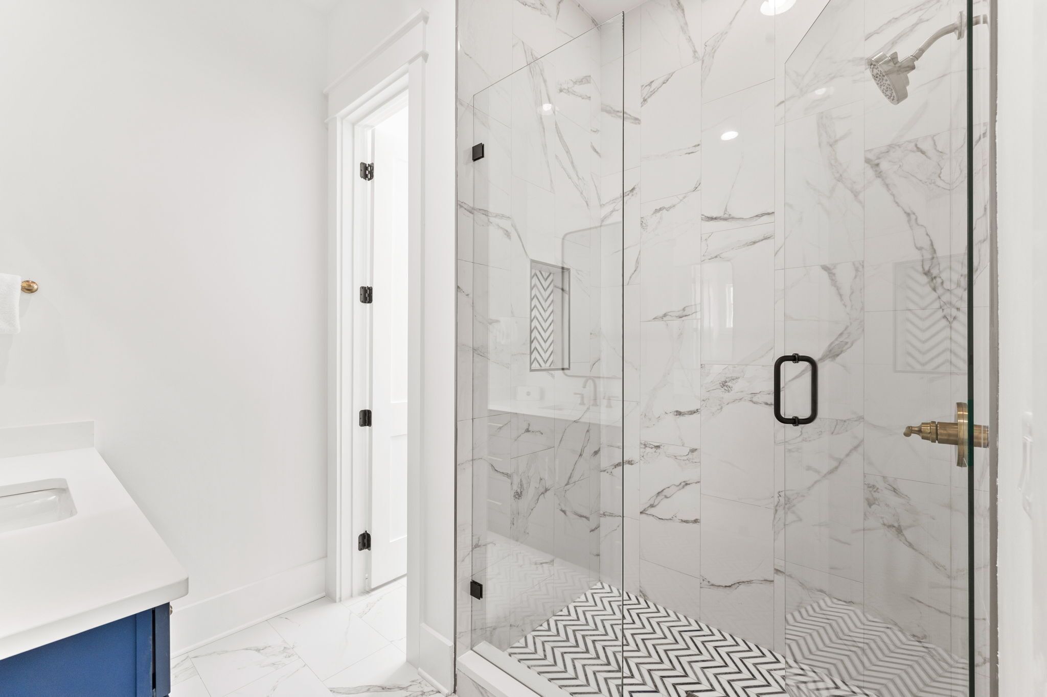 Een moderne badkamer met een douchecabine van glas, marmeren wanden en een witte wastafel.
