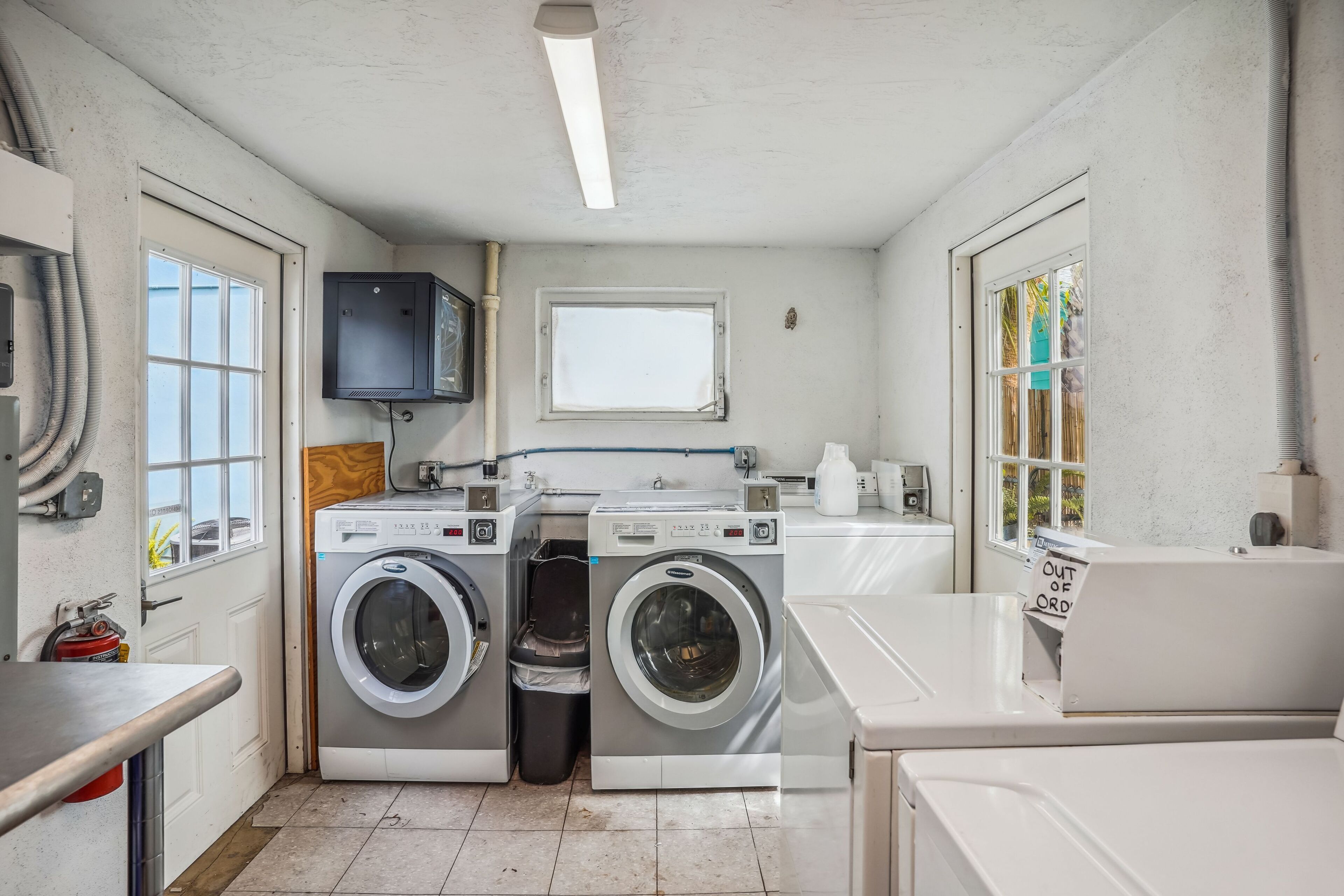 A laundry room with two front-loading washing machines, a dryer, a sink, and a window.